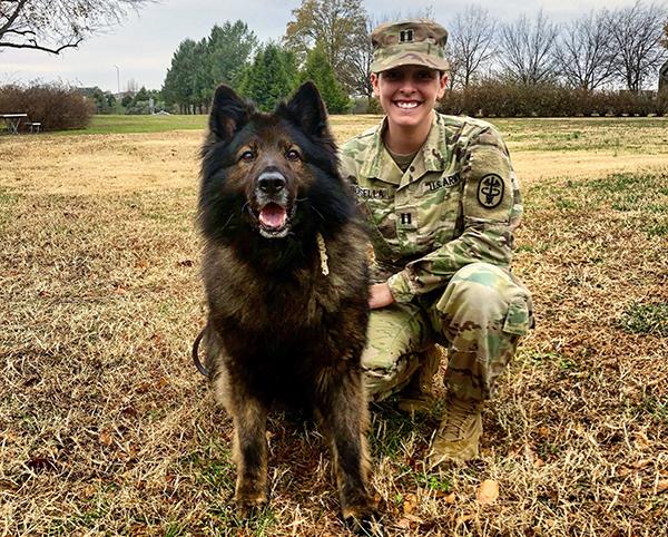 Major Kristen Arango kneels next to a military service dog named Terry